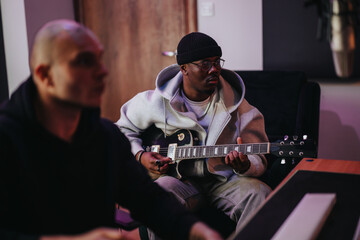 A focused music producer plays an electric guitar while collaborating in a recording studio. The...