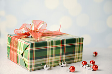  Festive plaid-wrapped gift with red ribbon surrounded by shiny ornaments.