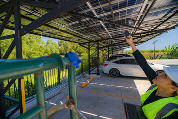 Female engineer inspecting solar panels on a carport while holding a laptop and infrared thermometer. Solar energy inspection, renewable energy technology, and clean energy infrastructure.