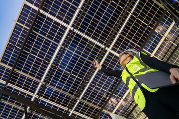 Technician inspects solar panels under a large solar carport structure. Focused on clean energy,...