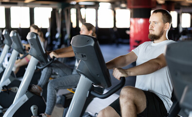 Young athletic man in sportswear training on exercise bike in gym