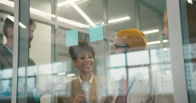 Team of professionals place sticky notes on glass wall