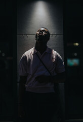 A person stands beneath a spotlight, casting deep shadows, highlighting the contemplative mood and...