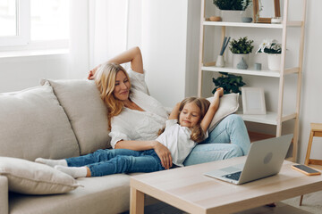 Joyful mother and daughter celebrating together on a cozy couch with arms raised in excitement and happiness