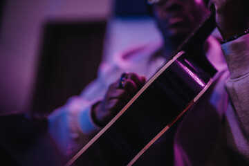 An artistic close-up of a musician strumming a guitar in dim, colorful lighting. This evocative image captures the soulful and expressive nature of playing music in an intimate setting.