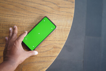 A hand reaches for a smartphone with a green screen on a table