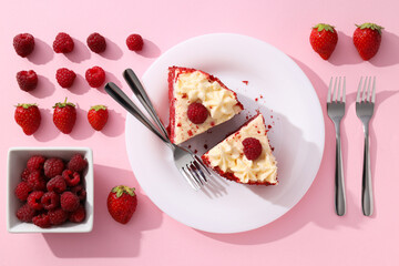 Pieces of red velvet cake on plate, berries and forks on pink background, top view
