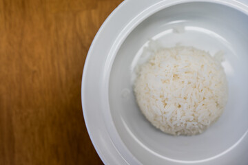 A white bowl of tasty cooked white rice on wood table