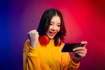 Asian young beautiful woman playing game on smartphone in neon background.