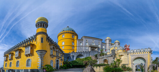 The vibrant yellow and grey Pena Palace stands majestically under a clear blue sky. The unique...