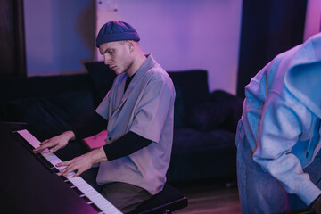 A young man is deeply focused on playing the piano in a dimly lit room. The soft lighting creates a...