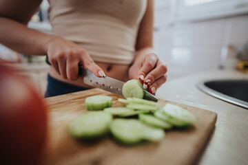 A woman slices cucumber on a wooden cutting board, showcasing healthy eating and home cooking. Her focus on preparation highlights the importance of fresh ingredients and mindful meal preparation.