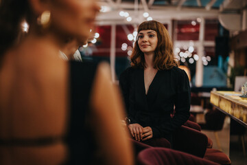 A young woman with a smile sitting in a trendy cafe during an evening gathering, surrounded by friends and warm ambient lighting.