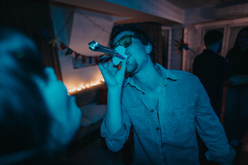 A young man wearing party accessories enthusiastically celebrates at a lively birthday party with...