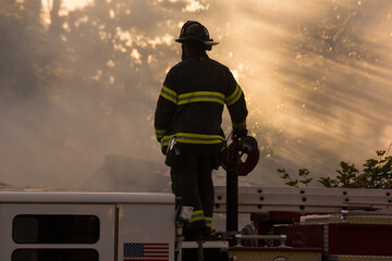 Firefighter standing on fire truck at house fire