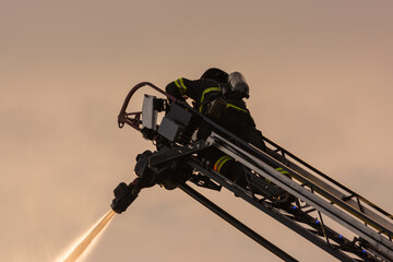 Firefighter pouring water on house fire from aerial ladder