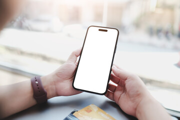 A person holding a smartphone with a blank screen, seated by a window with natural light. The scene emphasizes technology, simplicity, and a casual environment.