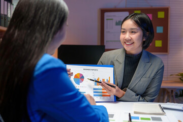 Two asian businesswomen are discussing business reports in an office meeting, pointing at charts and graphs