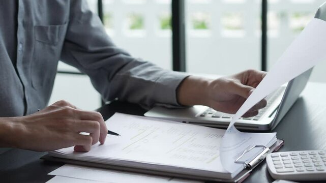 Businessman sits on chair holding pen and checking documents