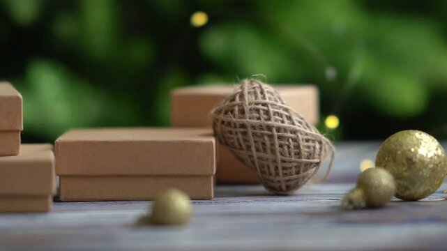 Holiday decor. Packing holiday gifts. Gift boxes and natural twine and Christmas gold balls on a Christmas tree background and bokeh. Moving focus across items