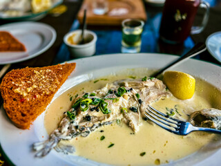 Fried Golden trout fish with lemon and herbs in a white plate on a wooden table at the restaurant in Ukraine