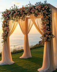 A beautiful floral arch adorned with pastel roses and draped fabric, set against a stunning sunset by the ocean.