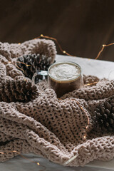 New Year, Christmas card. Coffee with milk in a glass mug among the cones on the blanket. Vertical photo