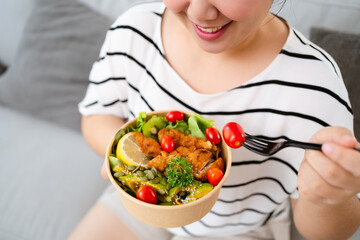 Beautiful Asian woman eating salad, holding a glass bowl and using a fork to pick up a tomato to eat