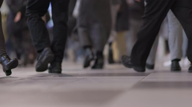 Low shot of legs and feet of people walking in a crowded Tokyo subway train station as a woman in black heels walks through during rush hour in slow motion. Captured at 120 frames per second.

