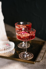 Two glasses of red wine with rose petals in them on a tray. Scene is elegant and sophisticated