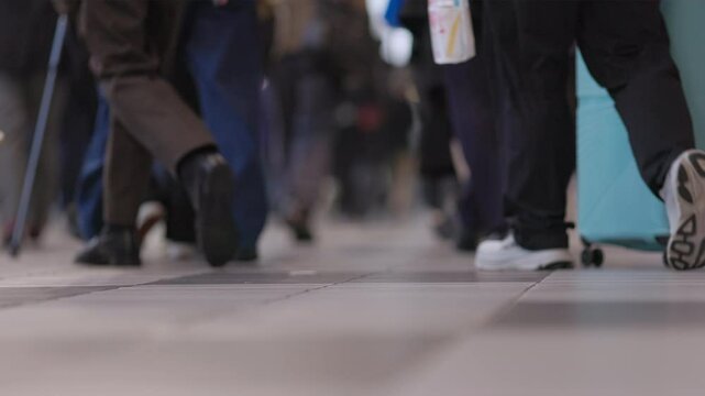 Low shot of legs and feet of people walking as a stroller rolls by in a crowded Tokyo subway train station during rush hour in slow motion circa 2024. Captured at 120 frames per second.

