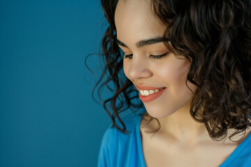 Portrait photo of a latina hispanic female model looking down at something with a smiling face isolated on a blue background