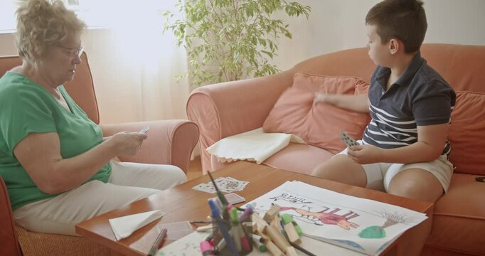 A grandmother and her grandson enjoy quality time together, playing cards in the living room. This heartwarming scene captures the essence of family bonds and inter generational connection.