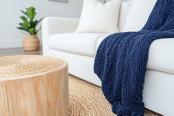 A cozy living room scene featuring a white sofa adorned with a navy blue knitted throw blanket. A round wooden coffee table with a textured surface sits in front of the sofa