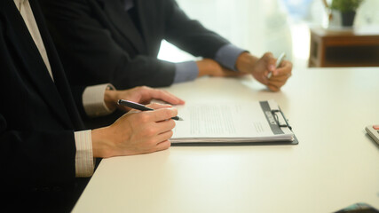 Professional businessman reviewing and signing formal agreement under the guidance of lawyer
