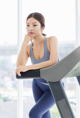 Asian young beautiful cheerful woman, active sport girl in sportswear exercise standing pose at treadmill training in fitness gym or living room smiling look at camera health care wellness lifestyle.