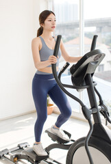Fototapeta premium Asian young beautiful cheerful happy woman active girl in sportswear stationary exercise bike movement speed energy training in fitness gym or living room at home, healthy wellness action lifestyle