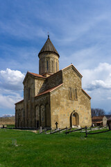 Samtavisi Cathedral in a courtyard with green grass. Stone walls with frescoes, orange tiled roof.