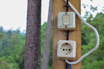 Outdoor Wooden Post with Electric Switches and Socket in a Forested Area