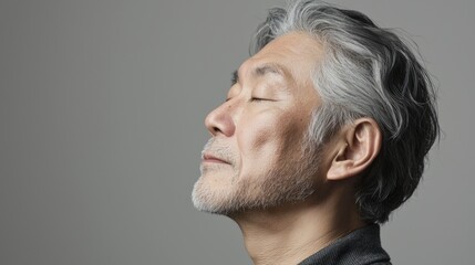 Fototapeta premium Photo of a mature, handsome Japanese man with gray hair, eyes closed in profile view on a gray background, with side lighting.generated ai 