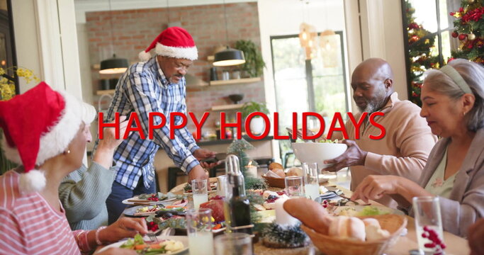 Image of happy holidays text over diverse senior friends at christmas dinner at home