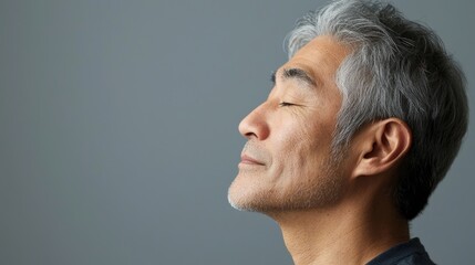 Fototapeta premium Photo of a mature, handsome Japanese man with gray hair, eyes closed in profile view on a gray background, with side lighting.generated ai 