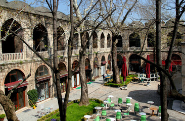 Courtyard view of the two-story Koza Han market with shops inside against a clear blue sky in Bursa, Turkey © Kateryna M