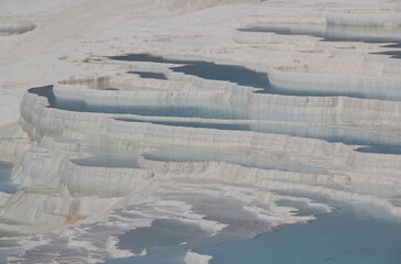 Fototapeta premium Rocky white travertines filled with blue water in Pamukkale, near Denizli, Turkey