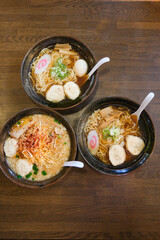 Three bowls of ramen soup sit on a table.