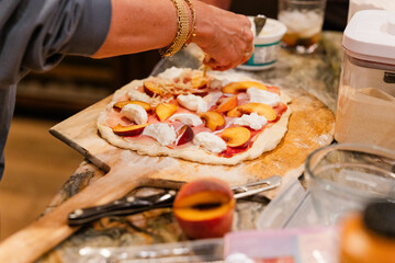 Adding cheese to a pizza with prosciutto, peaches, and ricotta