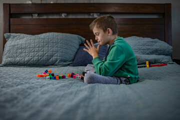 Boy sitting on a bed, focused on colorful toy blocks in front of him