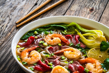 Shrimp and beef Pho soup - Vietnamese soup with shrimps and raw beef slices on wooden table	
