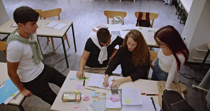 High school students collaborating on a project during class. They're using sticky notes, pens, a calculator and other supplies. Teamwork and studying together.