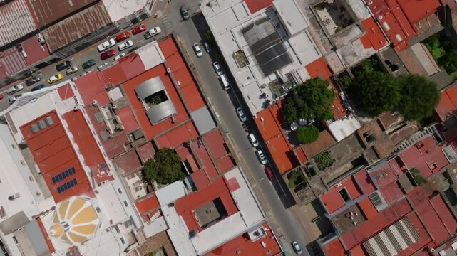 Aerial top down of Ciudad Guzman cityscape with traffic on main street. Solar panels on roof. Sunny day in Mexican town with park. Tilt up wide shot.